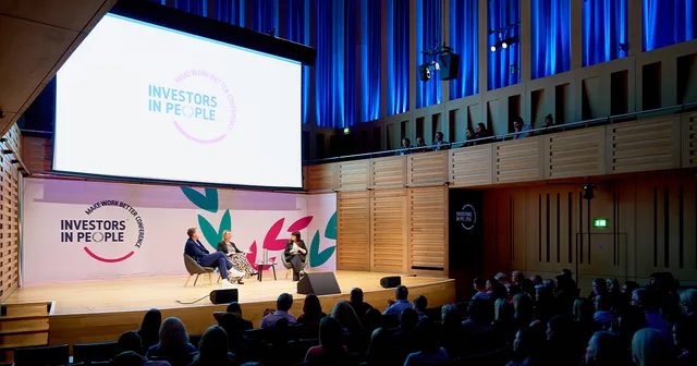 A fireside conversation on stage at the Make Work Better Conference 2026, in front of a full auditorium